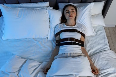 Photo of Sleepwalker fastened with belts lying in bed, above view