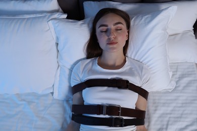 Photo of Sleepwalker fastened with belts lying on bed, top view