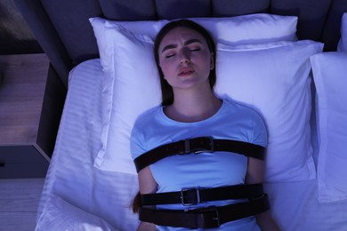 Photo of Sleepwalker fastened with belts lying on bed, top view