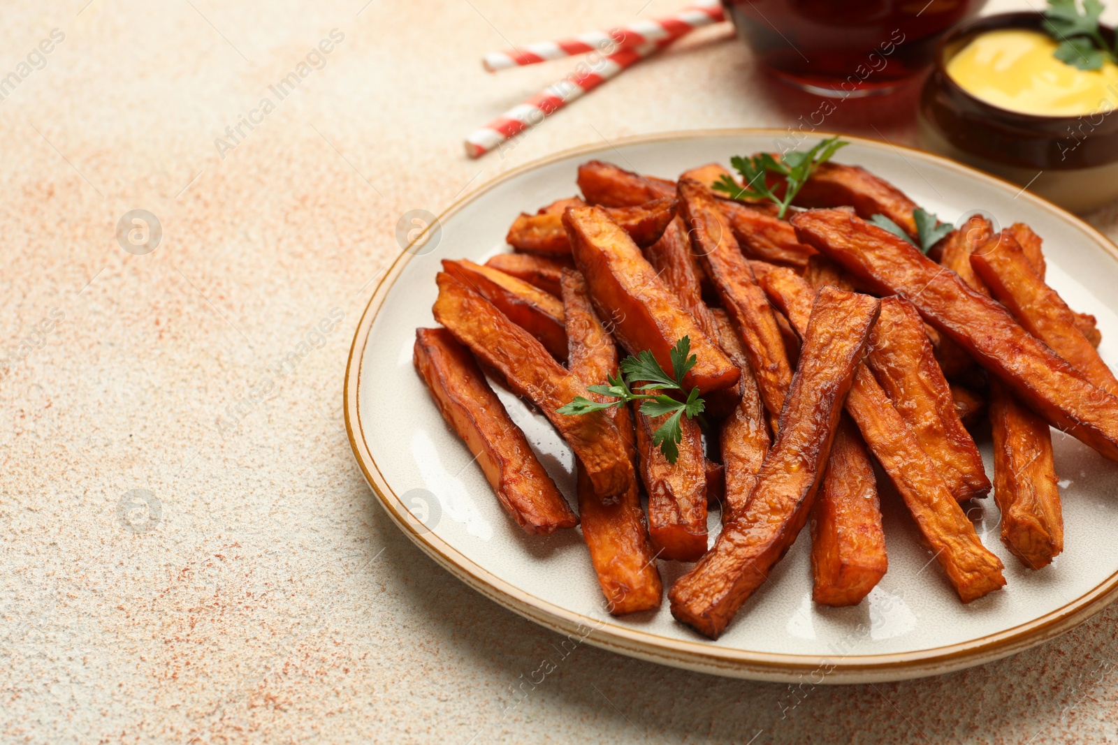 Photo of Delicious sweet potato fries, parsley and sauce on beige textured table, closeup. Space for text