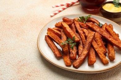 Photo of Delicious sweet potato fries, parsley and sauce on beige textured table, closeup. Space for text