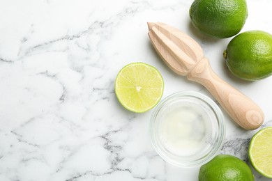 Photo of Wooden juicer and fresh limes on white marble table, flat lay. Space for text