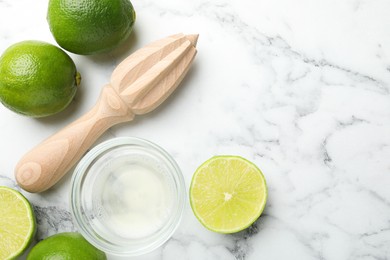 Photo of Wooden juicer and fresh limes on white marble table, flat lay. Space for text