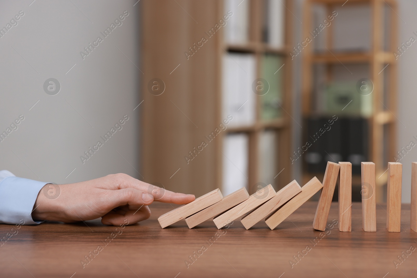 Photo of Domino effect. Woman pushing wooden blocks at table, closeup