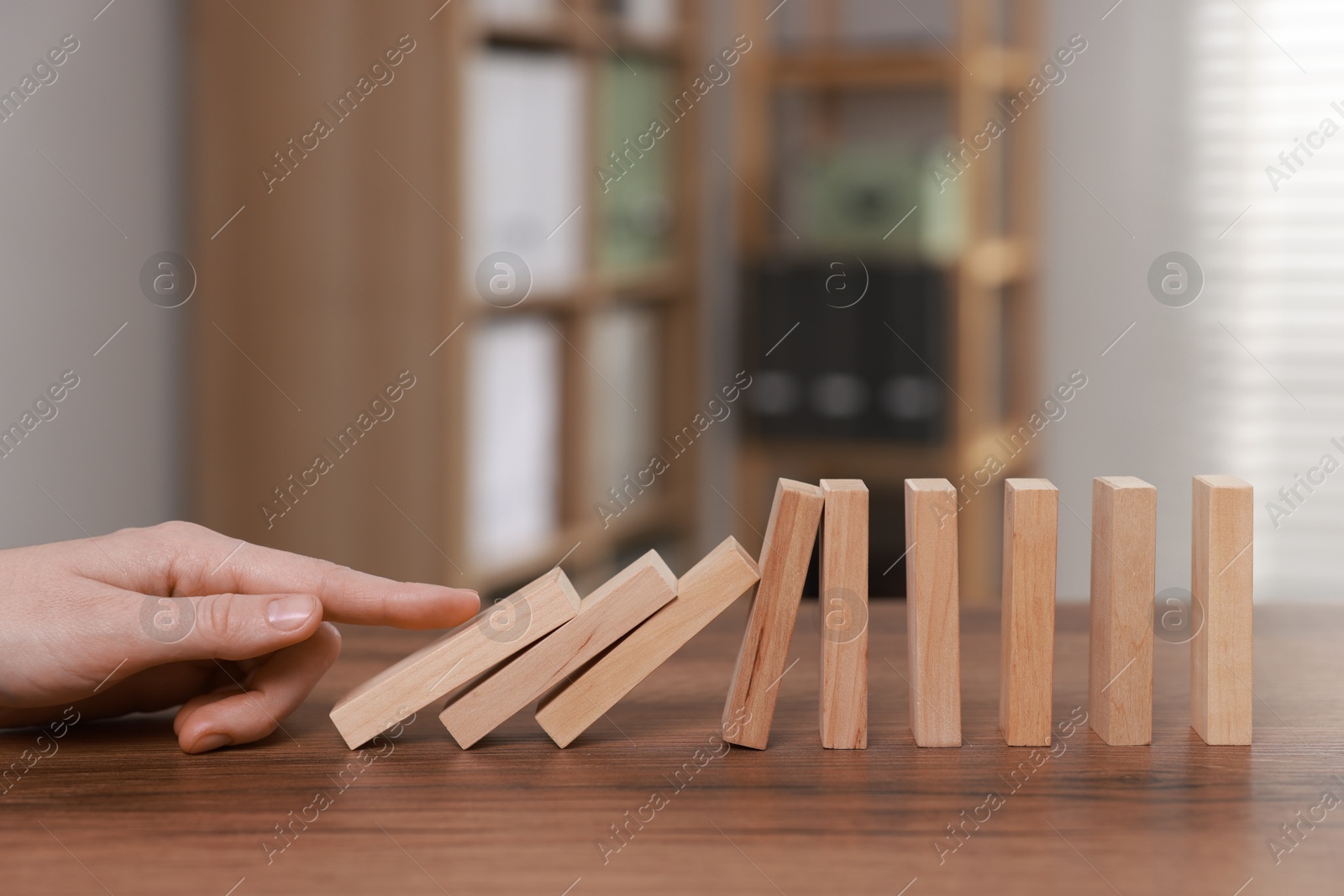 Photo of Domino effect. Woman pushing wooden blocks at table, closeup