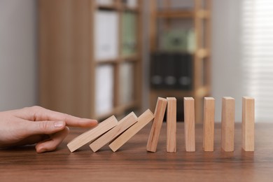 Photo of Domino effect. Woman pushing wooden blocks at table, closeup