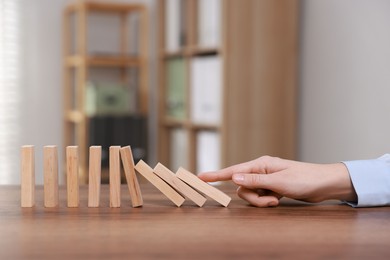 Photo of Domino effect. Woman pushing wooden blocks at table, closeup