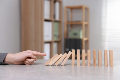 Photo of Domino effect. Woman pushing wooden blocks at table, closeup