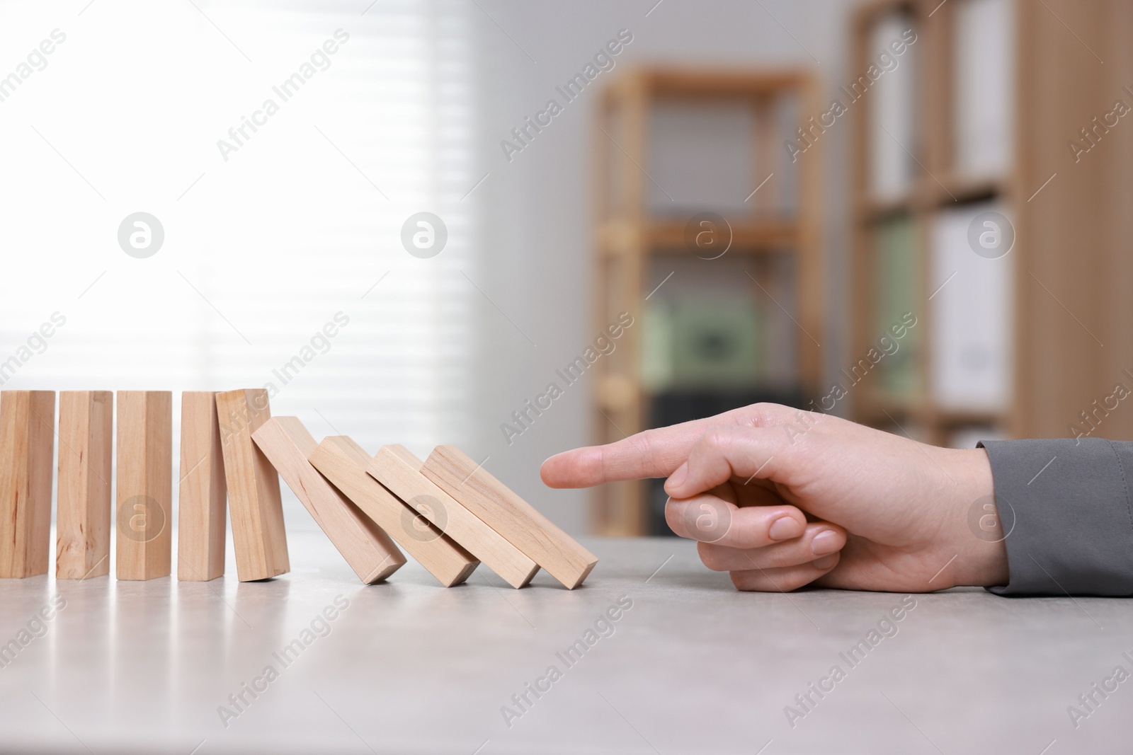 Photo of Domino effect. Woman pushing wooden blocks at table, closeup