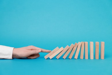 Photo of Domino effect. Woman pushing wooden blocks on light blue background, closeup