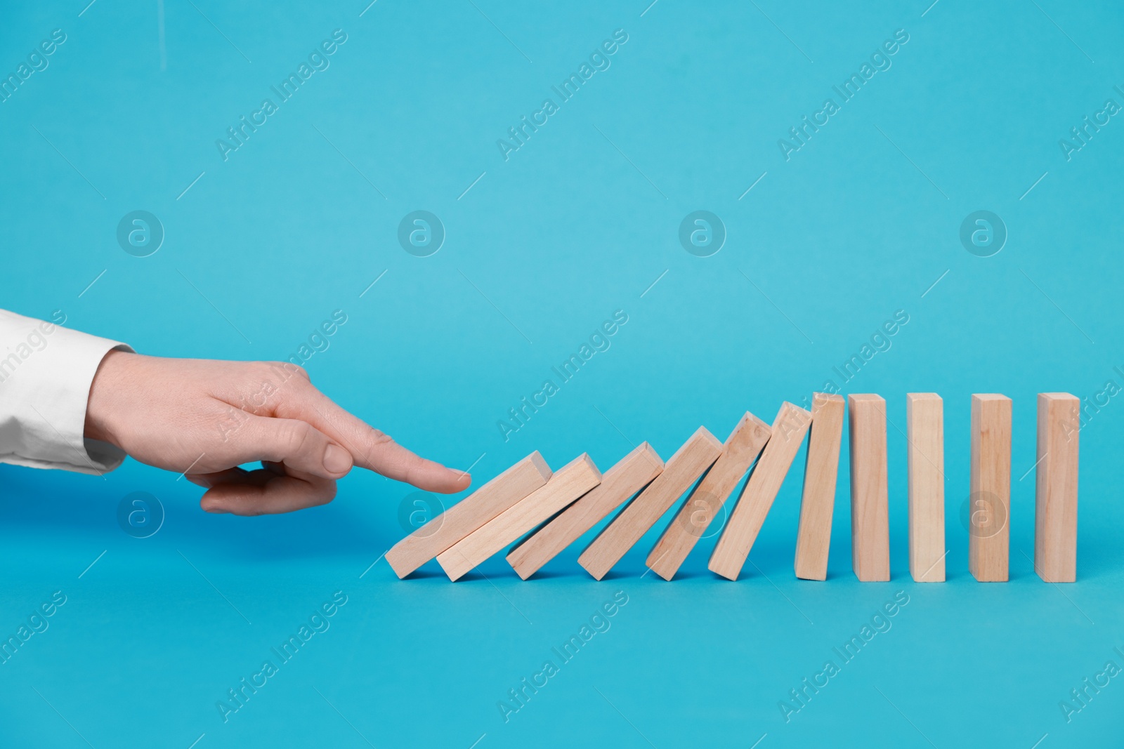 Photo of Domino effect. Woman pushing wooden blocks on light blue background, closeup