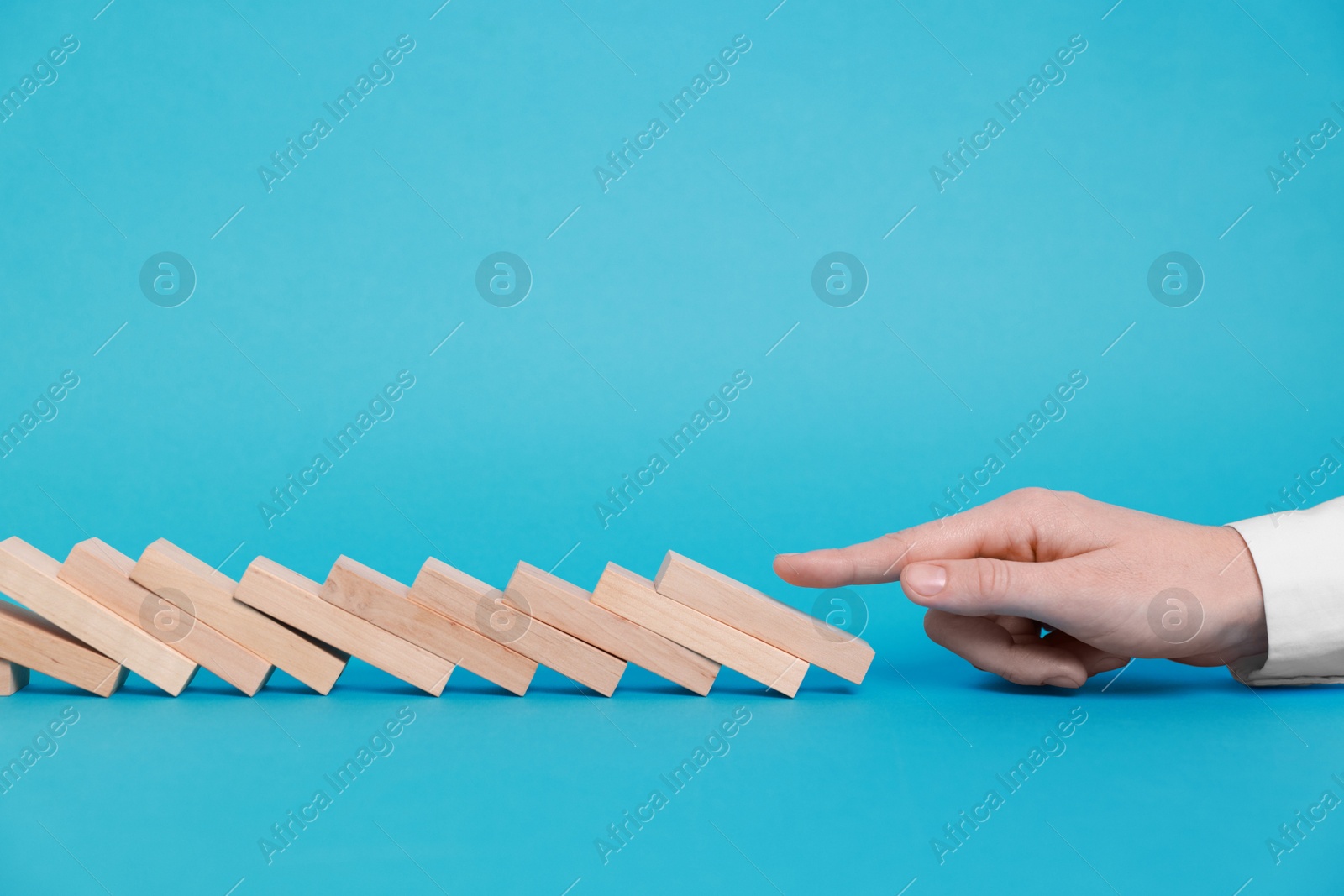 Photo of Domino effect. Woman pushing wooden blocks on light blue background, closeup