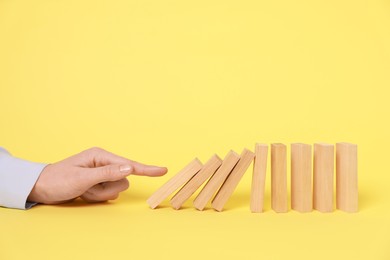 Photo of Domino effect. Woman pushing wooden blocks on yellow background, closeup