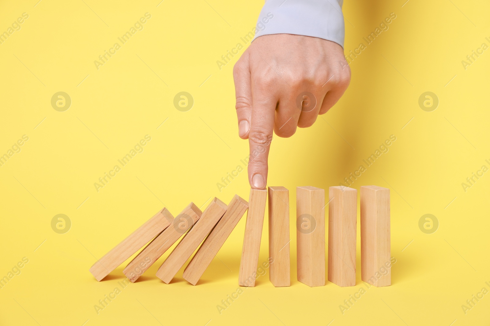 Photo of Domino effect. Woman pushing wooden blocks on yellow background, closeup