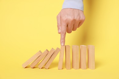 Photo of Domino effect. Woman pushing wooden blocks on yellow background, closeup