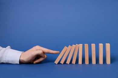 Photo of Domino effect. Woman pushing wooden blocks on blue background, closeup