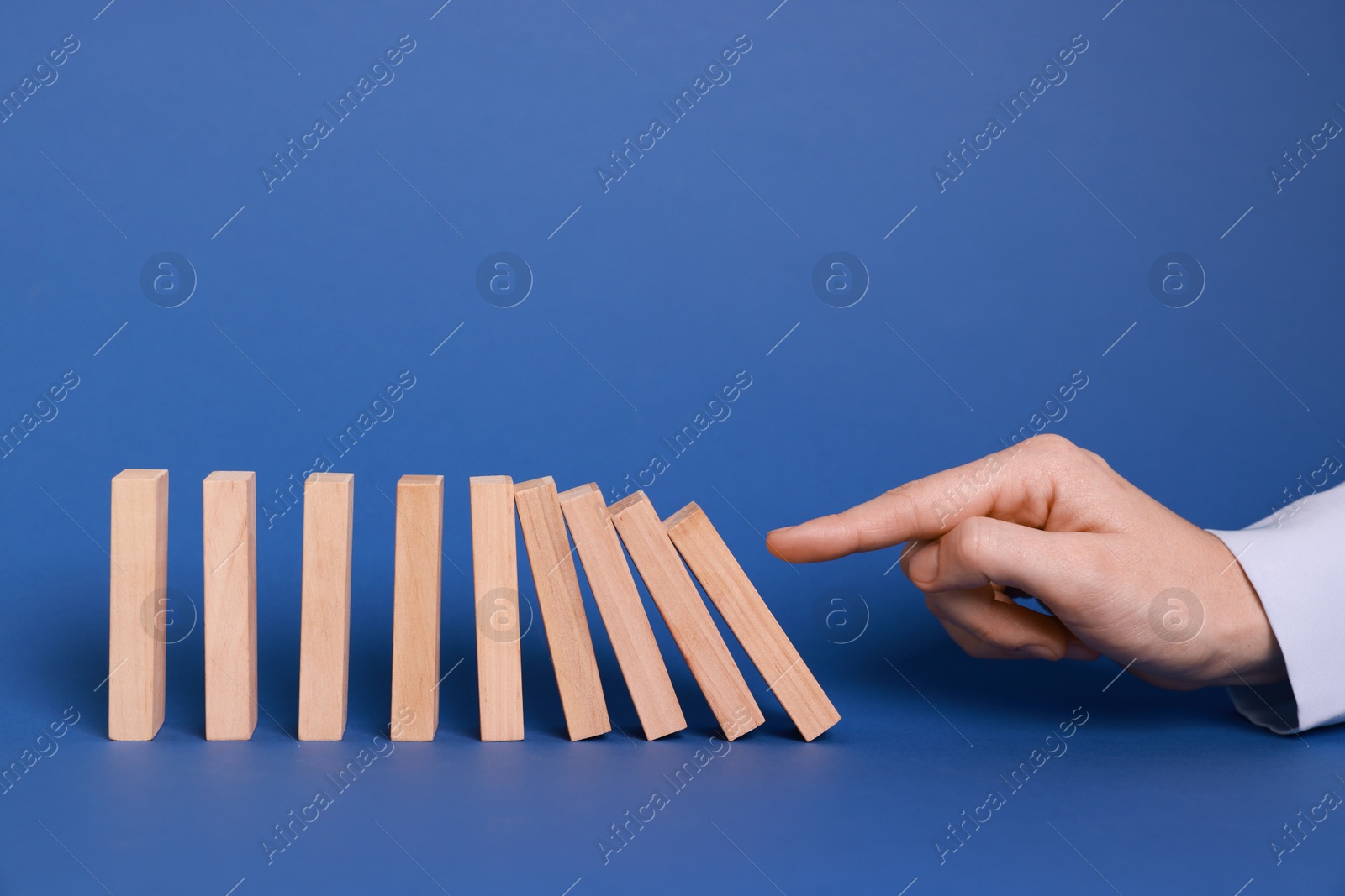 Photo of Domino effect. Woman pushing wooden blocks on blue background, closeup