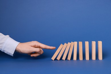 Photo of Domino effect. Woman pushing wooden blocks on blue background, closeup