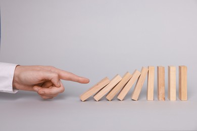 Photo of Domino effect. Woman pushing wooden blocks on light background, closeup