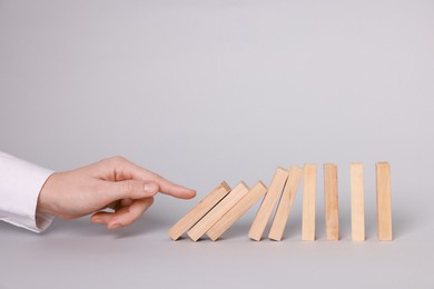 Photo of Domino effect. Woman pushing wooden blocks on light background, closeup