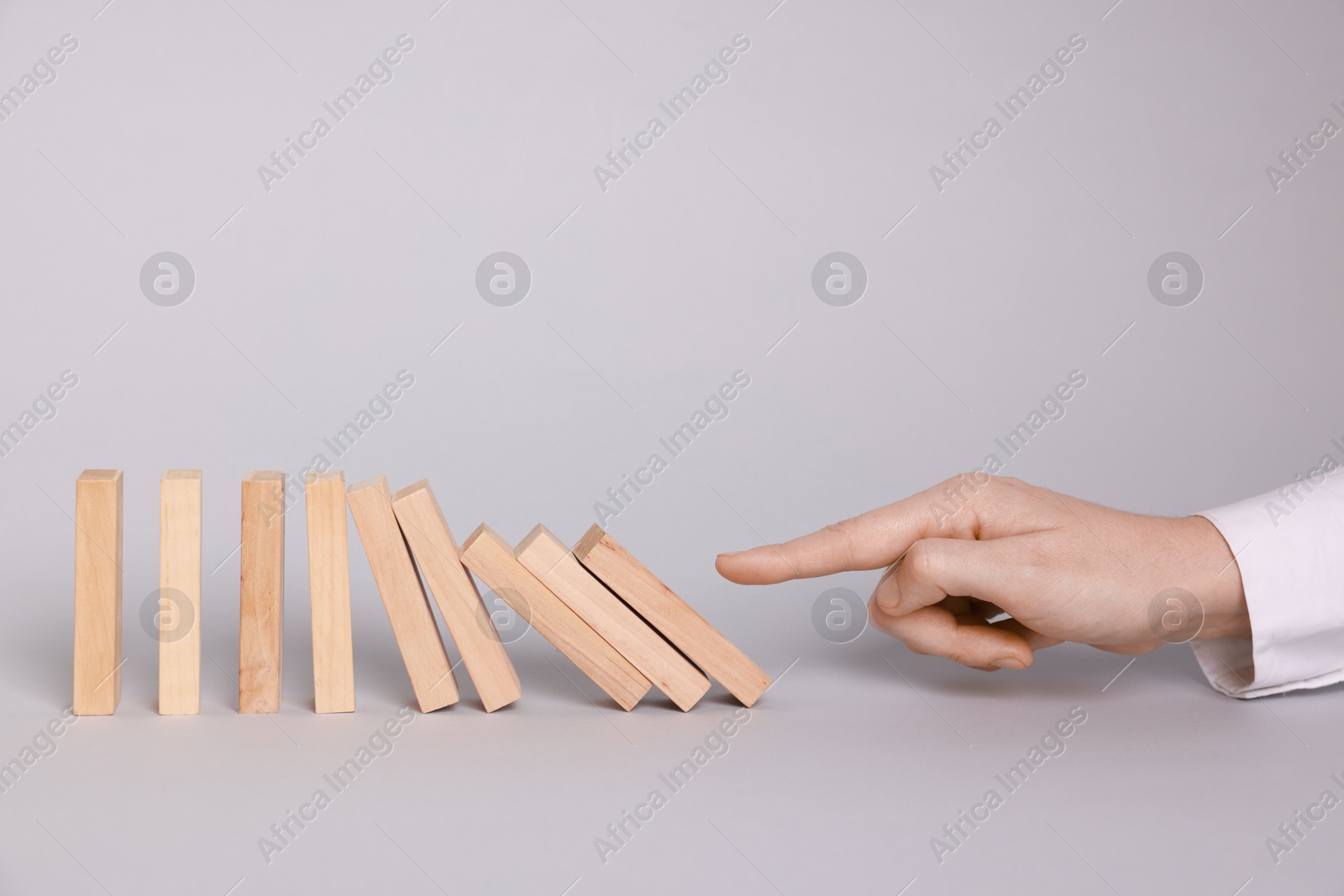 Photo of Domino effect. Woman pushing wooden blocks on light background, closeup