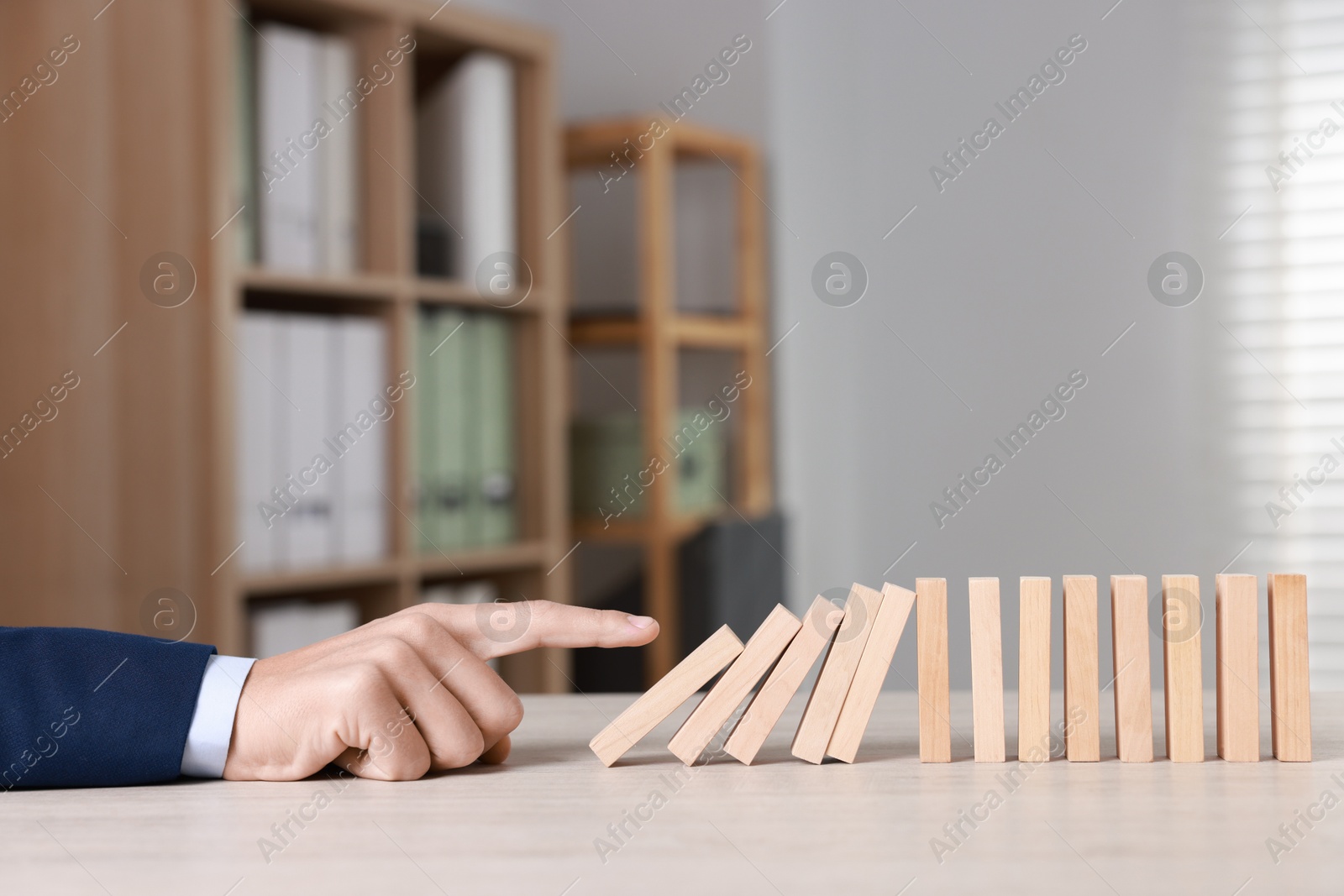 Photo of Domino effect. Man pushing wooden blocks at table, closeup