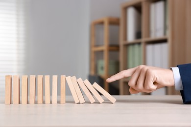 Photo of Domino effect. Man pushing wooden blocks at table, closeup