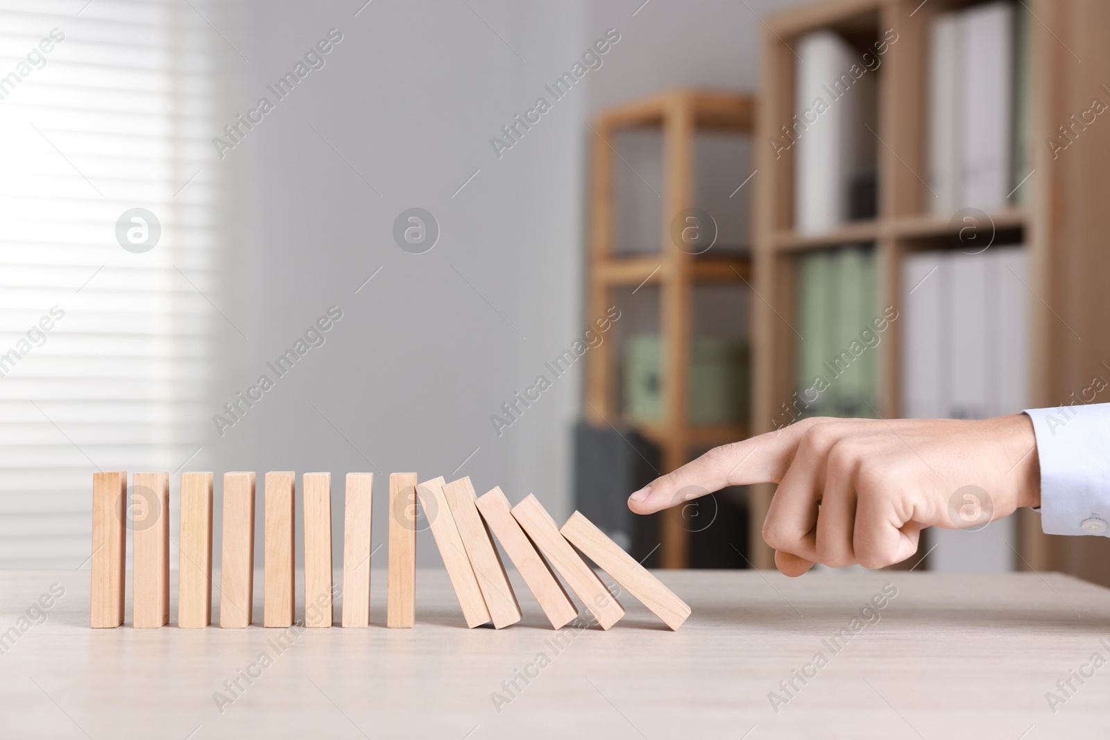 Photo of Domino effect. Man pushing wooden blocks at table, closeup