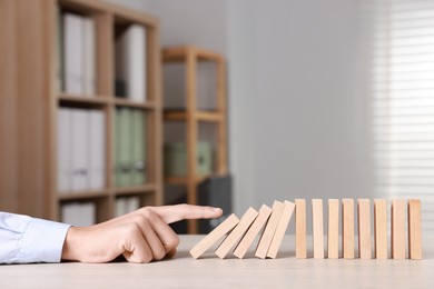 Photo of Domino effect. Man pushing wooden blocks at table, closeup