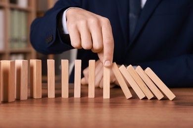 Photo of Domino effect. Man pushing wooden blocks at table, closeup