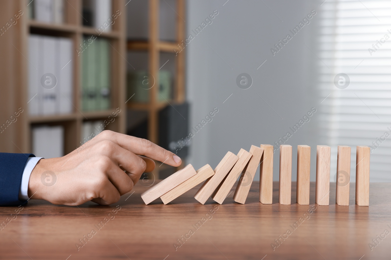 Photo of Domino effect. Man pushing wooden blocks at table, closeup