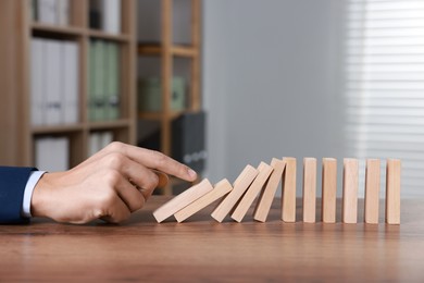 Photo of Domino effect. Man pushing wooden blocks at table, closeup