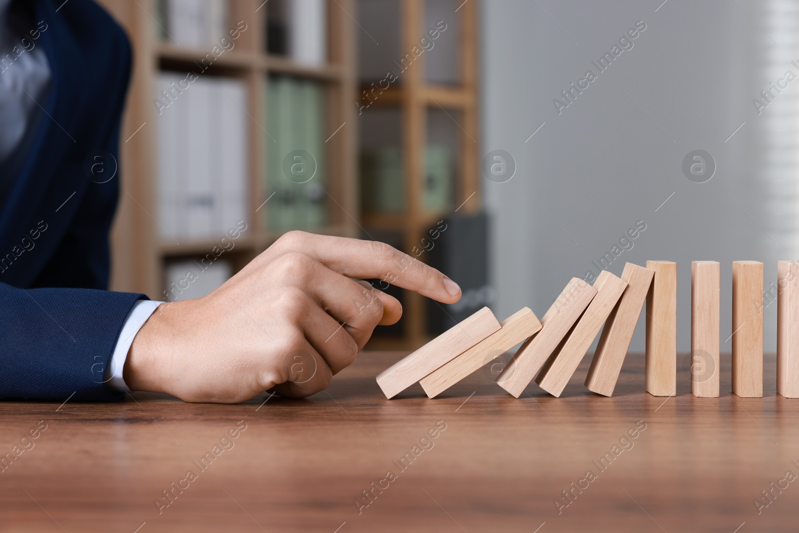 Photo of Domino effect. Man pushing wooden blocks at table, closeup