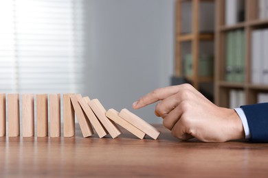 Photo of Domino effect. Man pushing wooden blocks at table, closeup