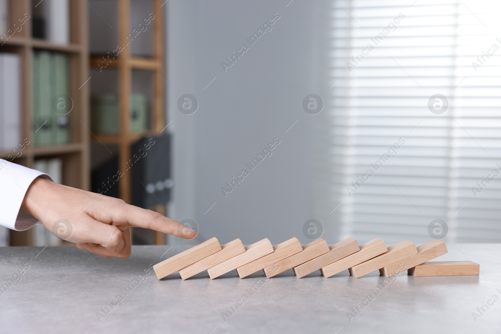 Photo of Domino effect. Man pushing wooden blocks at table, closeup