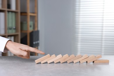 Photo of Domino effect. Man pushing wooden blocks at table, closeup