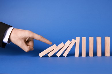 Photo of Domino effect. Man pushing wooden blocks on blue background, closeup