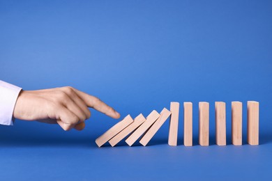 Photo of Domino effect. Man pushing wooden blocks on blue background, closeup