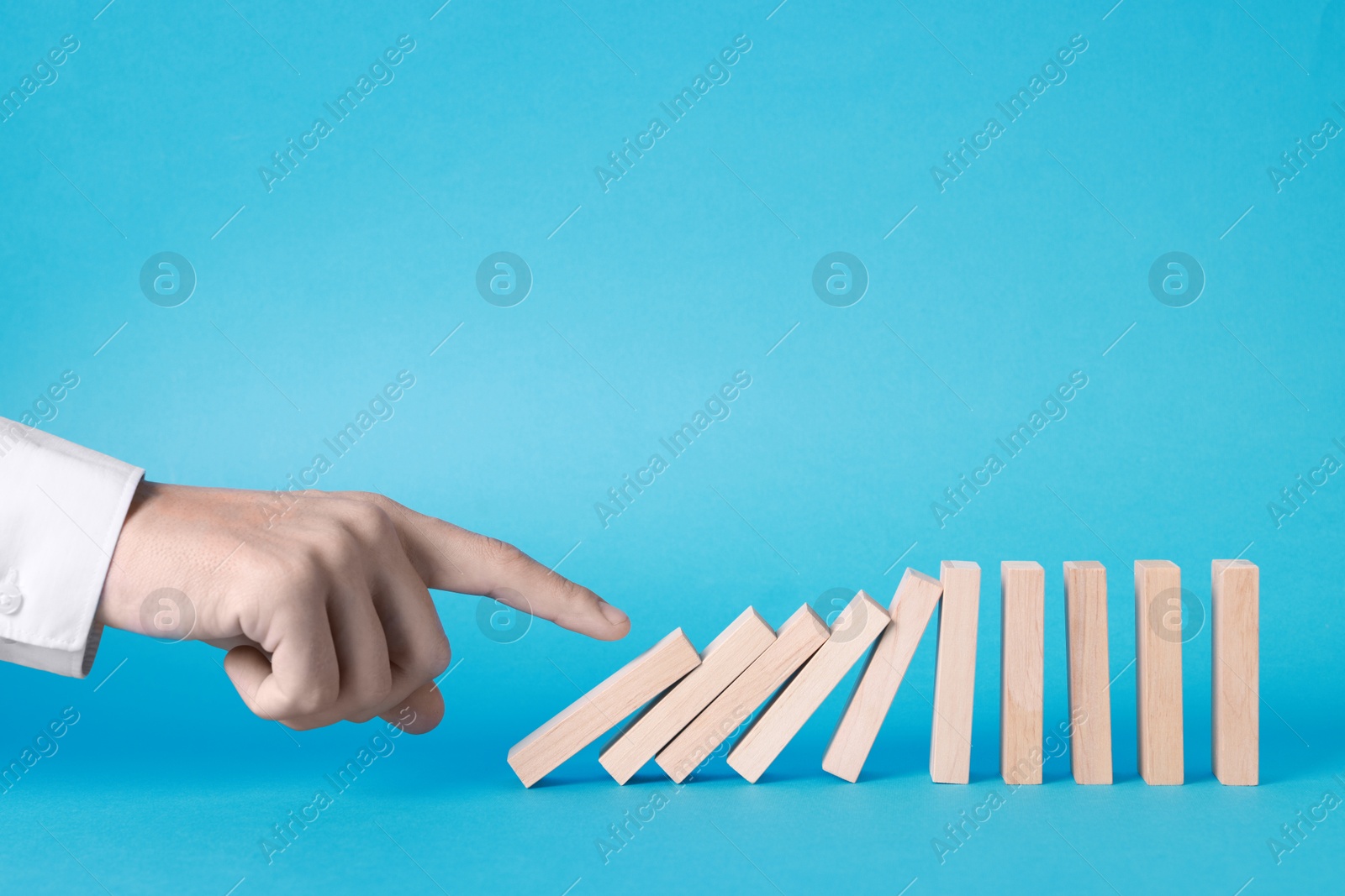 Photo of Domino effect. Man pushing wooden blocks on light blue background, closeup