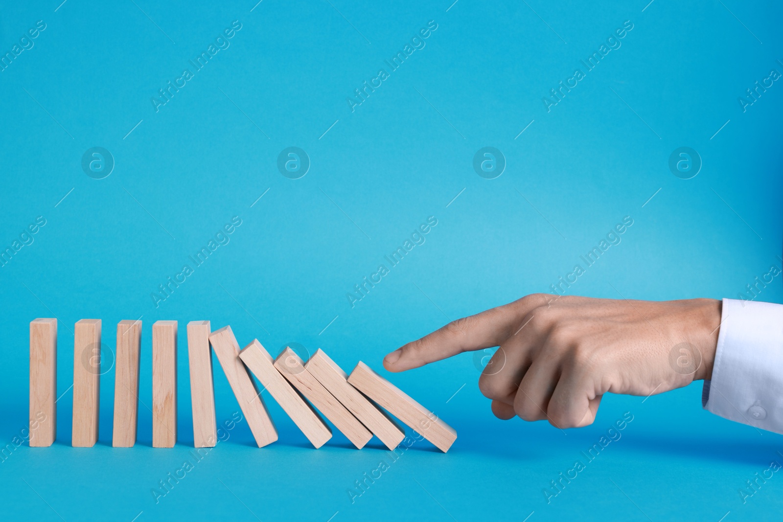 Photo of Domino effect. Man pushing wooden blocks on light blue background, closeup