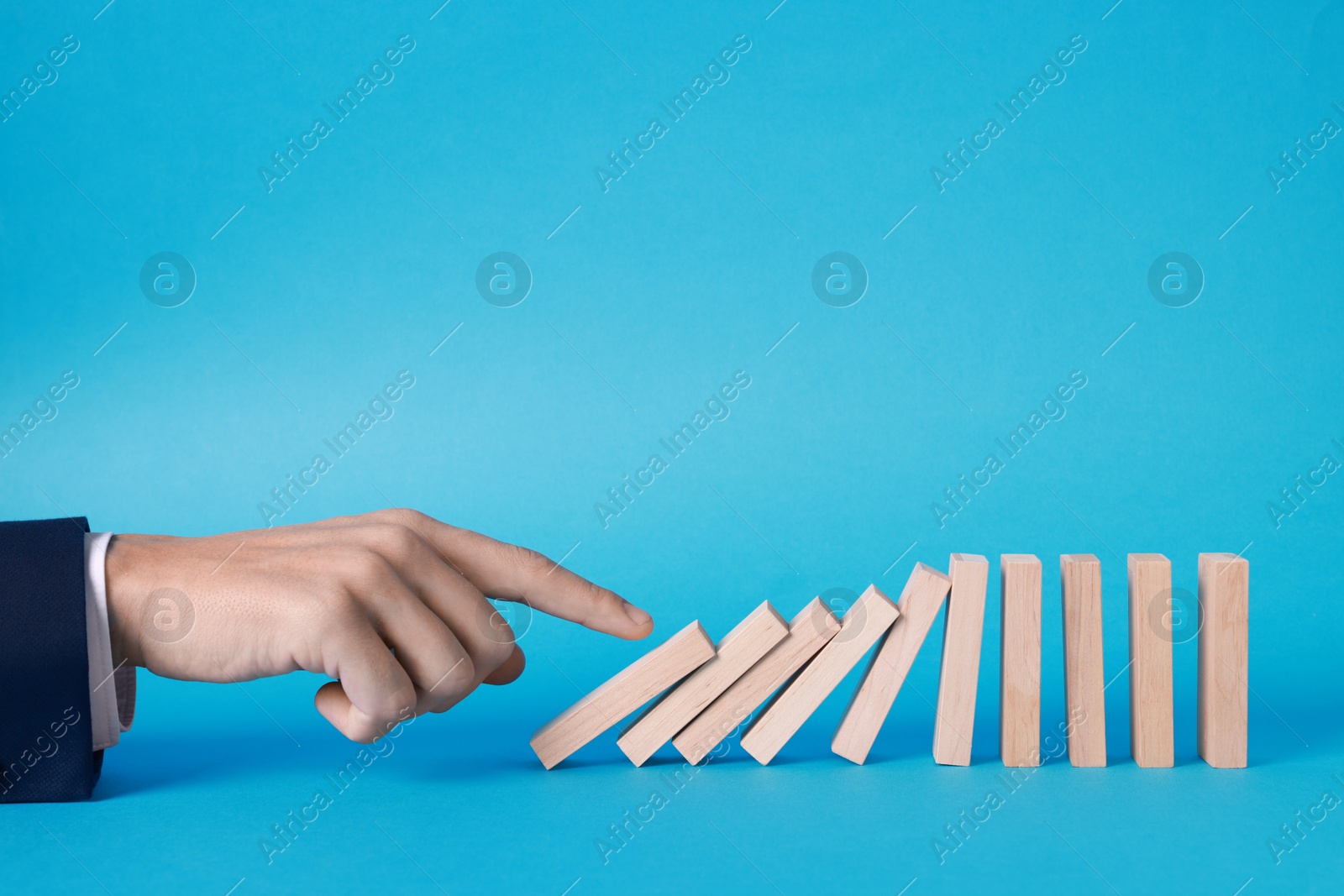 Photo of Domino effect. Man pushing wooden blocks on light blue background, closeup