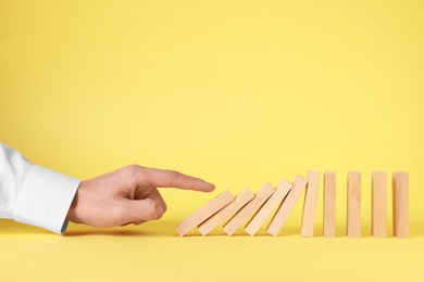 Photo of Domino effect. Man pushing wooden blocks on yellow background, closeup