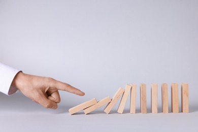 Photo of Domino effect. Man pushing wooden blocks on light background, closeup