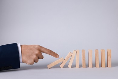 Photo of Domino effect. Man pushing wooden blocks on light background, closeup