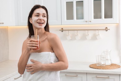 Photo of Spa day. Beautiful woman with face mask and juice in kitchen, space for text