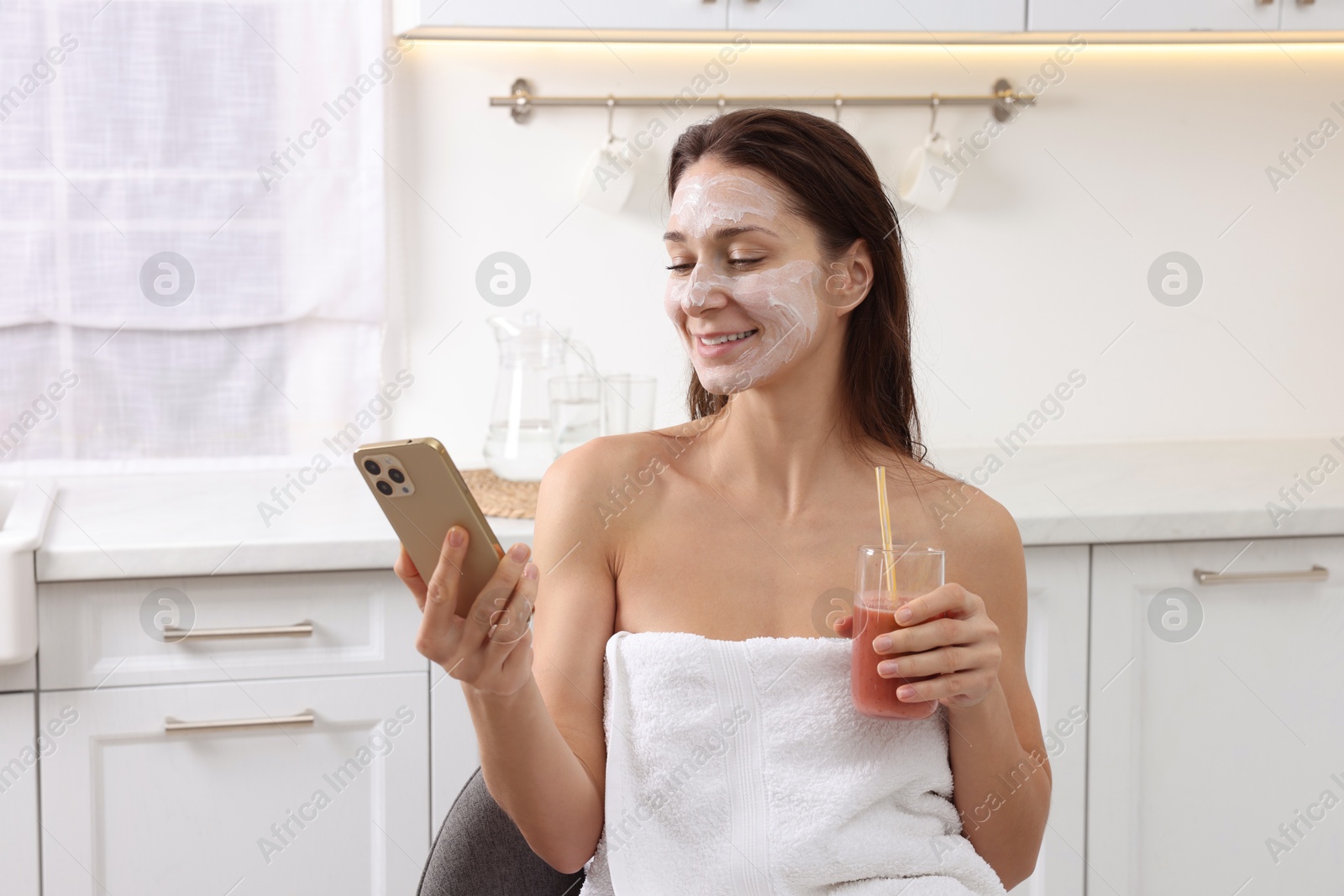 Photo of Spa day. Beautiful woman with face mask and juice using smartphone in kitchen