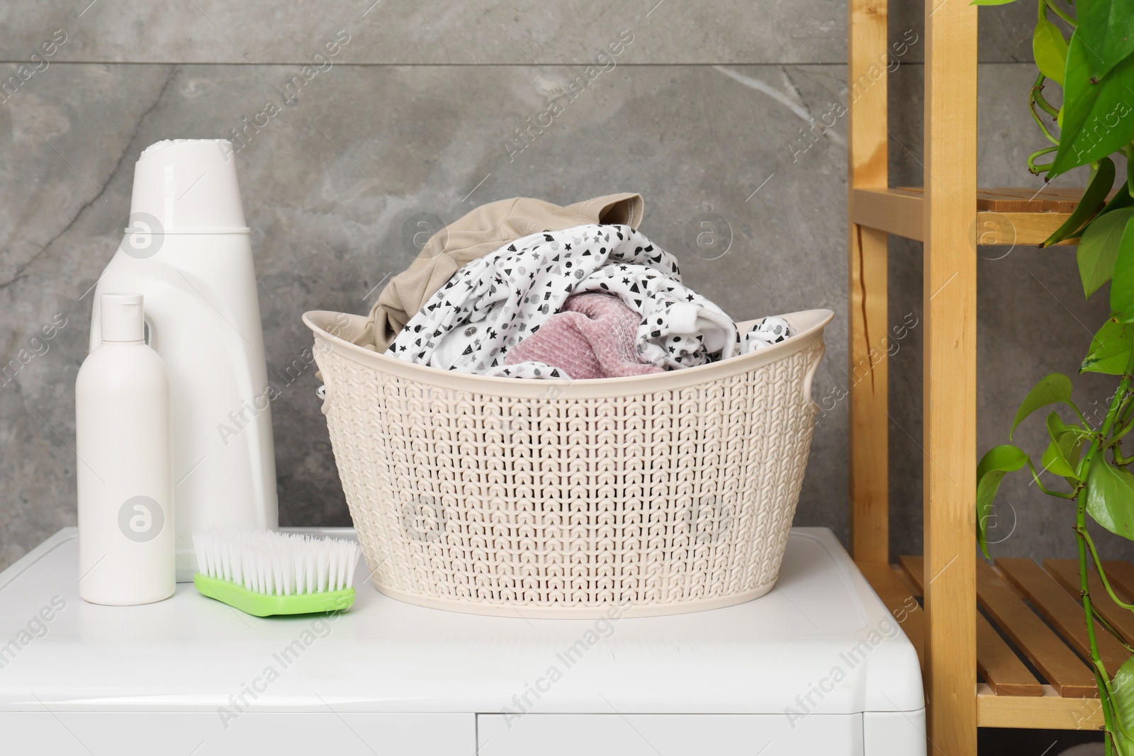 Photo of Detergents, brush and basket with laundry on washing machine indoors