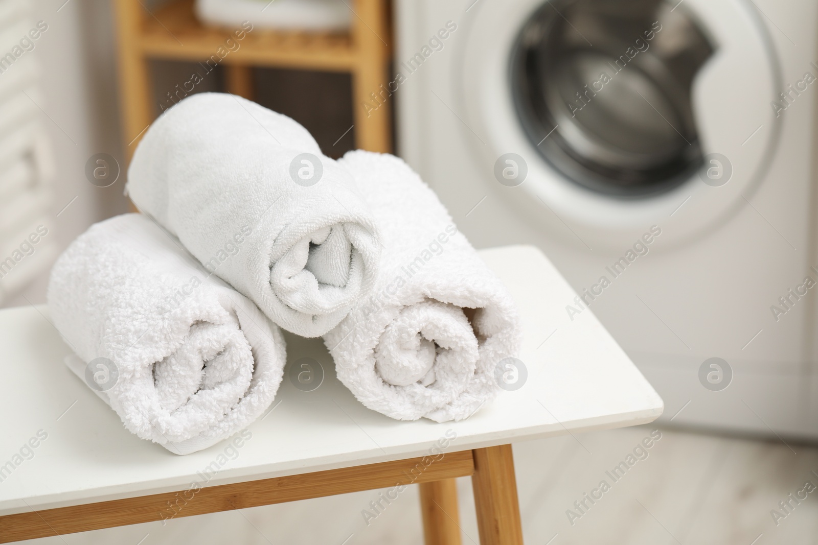 Photo of Rolled terry towels on white table in laundry room. Space for text