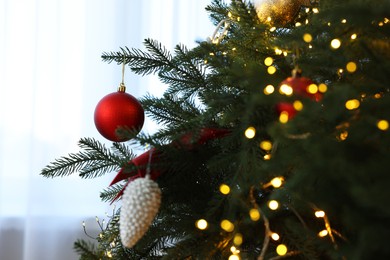 Photo of Christmas tree decorated with beautiful ornaments and lights indoors, closeup