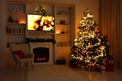 Photo of Blurred view of beautifully decorated Christmas tree near fireplace in room. Festive interior design